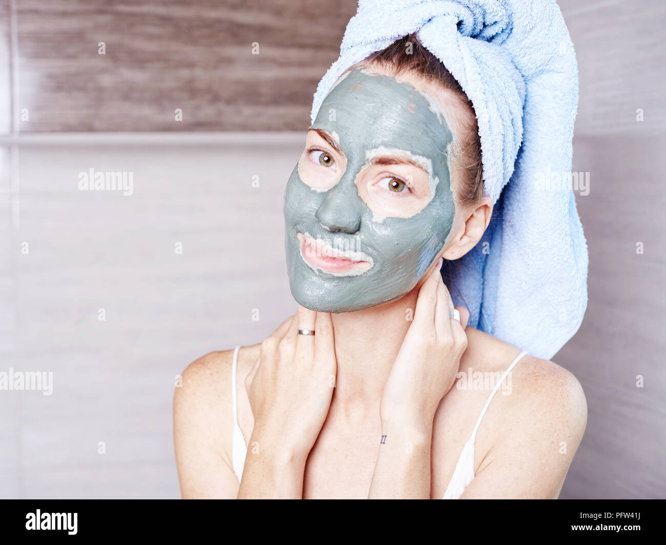 Woman applying mask moisturizing skin cream on face looking in bathroom