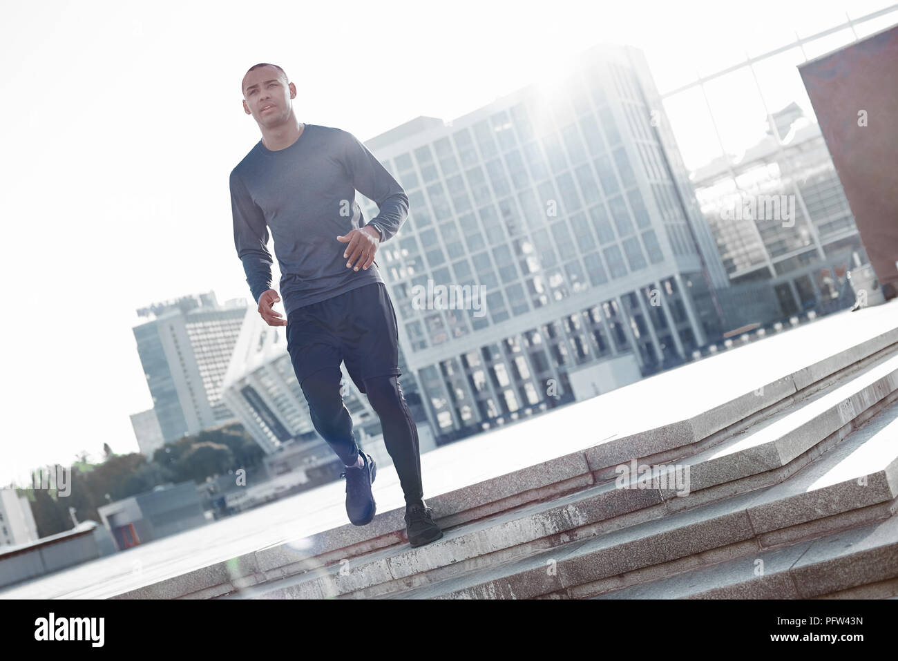 Urban sports. Latin american athlete running in city at morning Stock