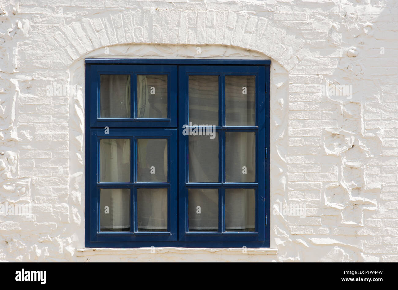 Blue painted wooden window frame set in whitewashed brick and stone wall. Stock Photo
