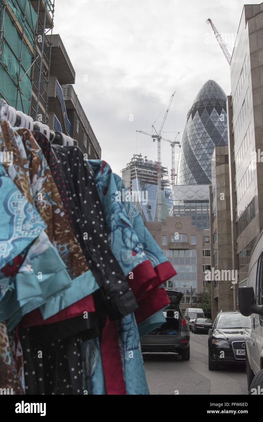 A street view, shot from a low angle, with a rack of brightly colored satin robes or kimonos in the left foreground, and construction near London's Gherkin building in the background, photographed at Petticoat Lane Market, located in the East End, in London, England, October 29, 2017. () Stock Photo