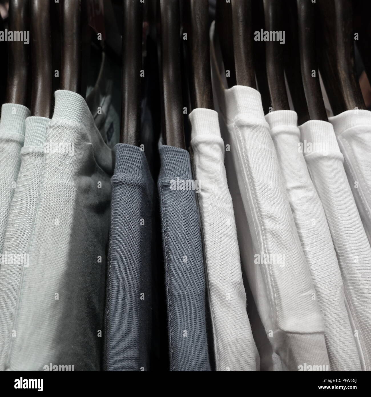 Selection of white and grey mens t shirts hanging on hangers on a rack in a fashion store or shop Stock Photo