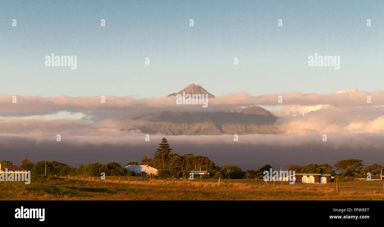 Mount Taranaki emerges from the clouds. One of New Zealand's classic scenes captured at sunset from the Freedom Camping Park at Opunake Beach Stock Photo