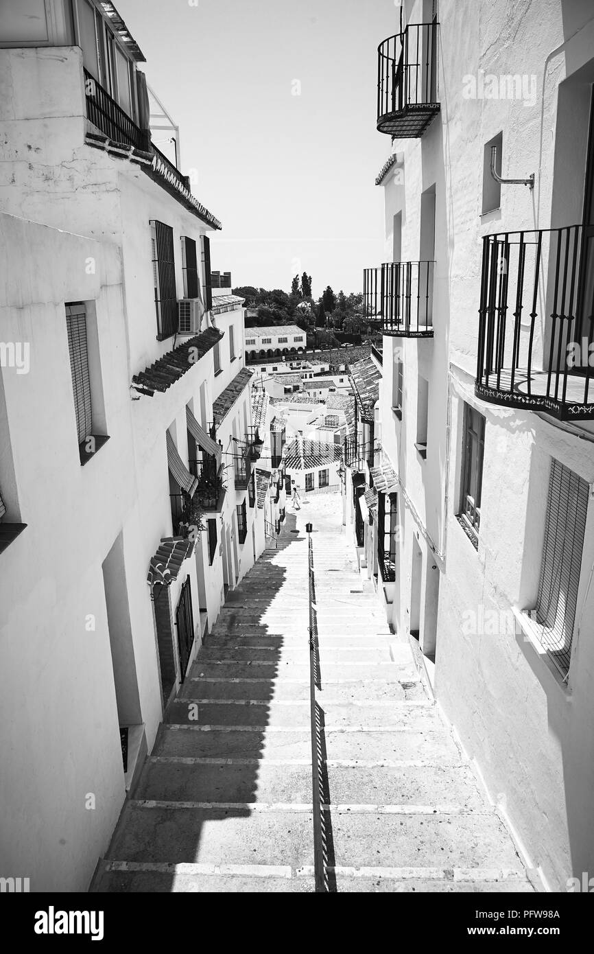 Black and white photo looking down the steps of a narrow Spanish street of white walled houses in Mijas, Andalusia in southern Spain Stock Photo