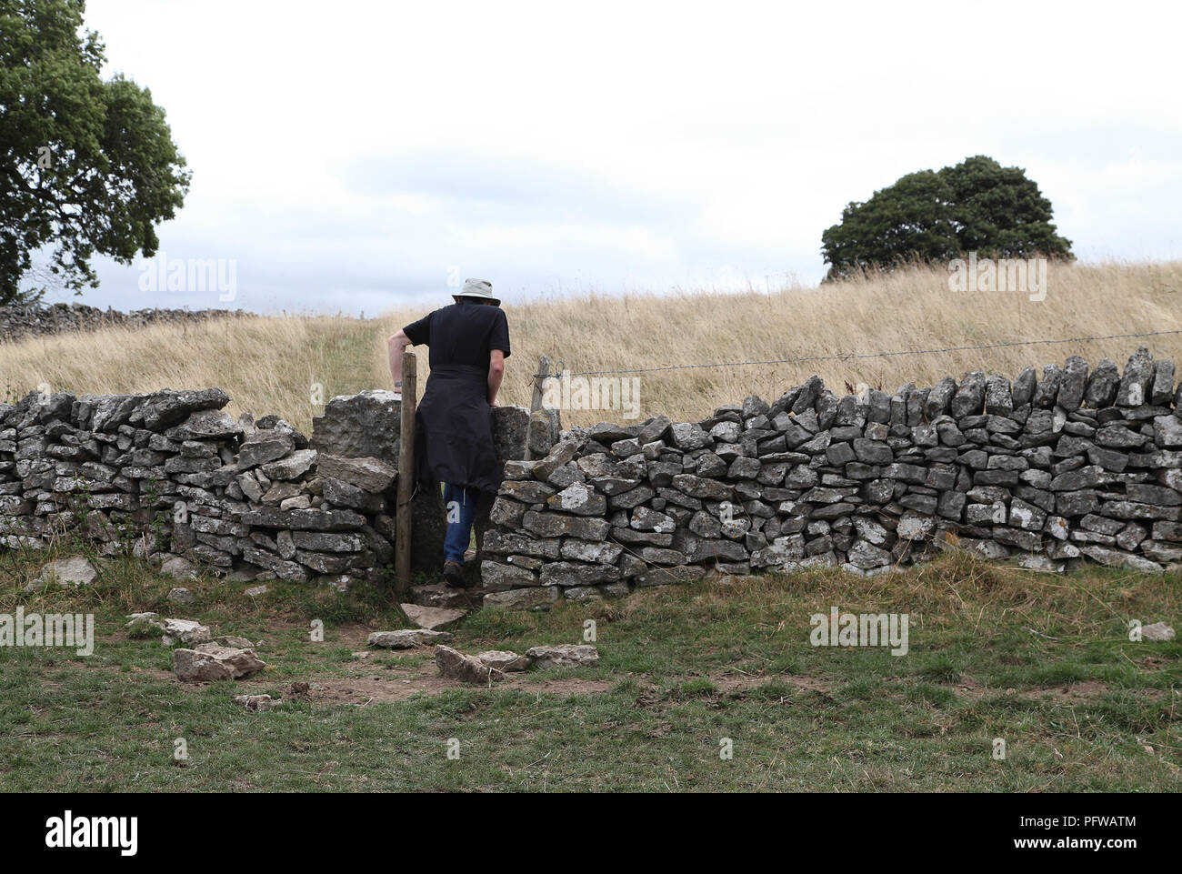 Walker in the Derbyshire countryside with a squeeze stile in a dry stone wall Stock Photo