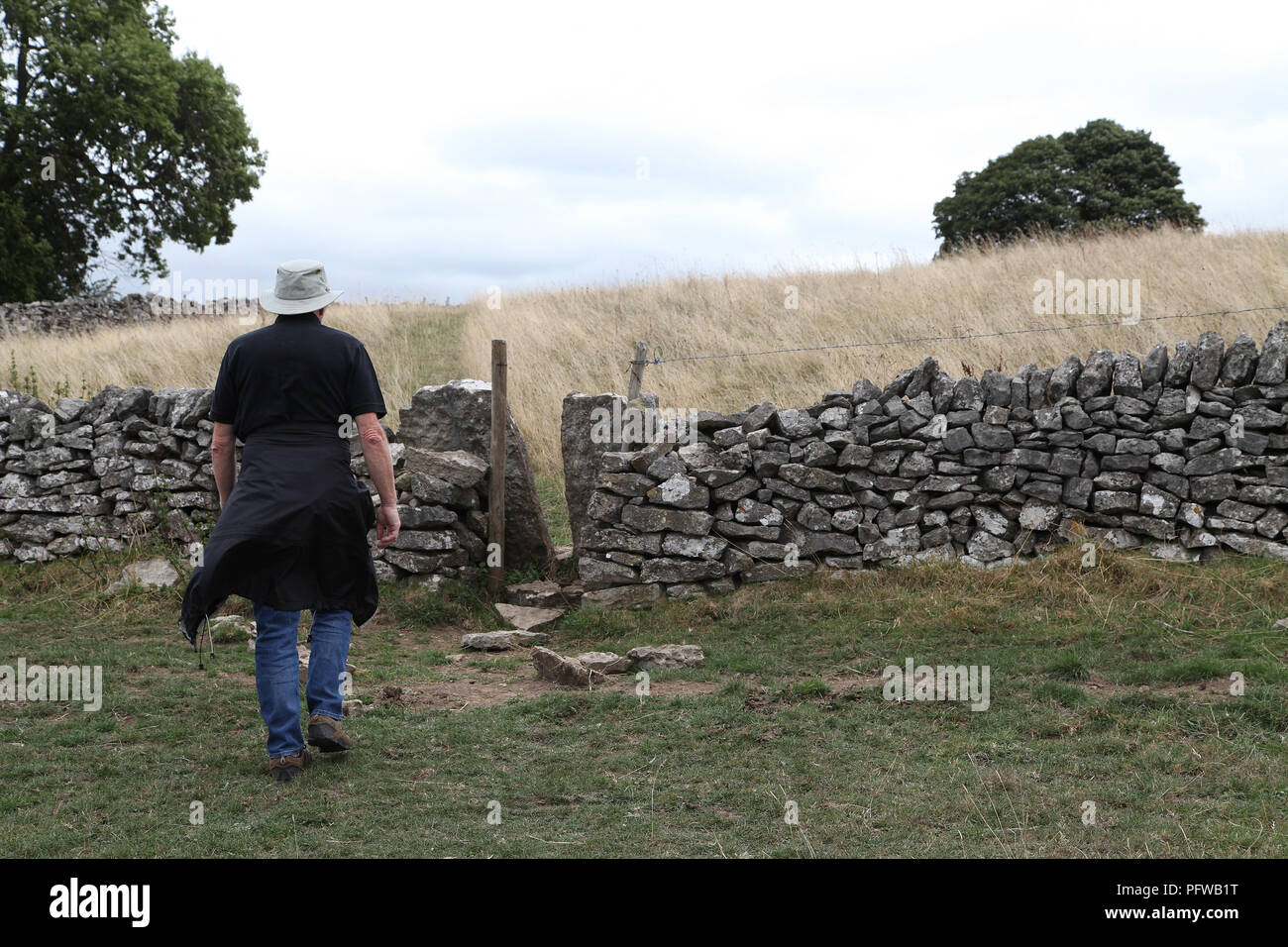 Walker in the Derbyshire countryside with a squeeze stile in a dry stone wall Stock Photo