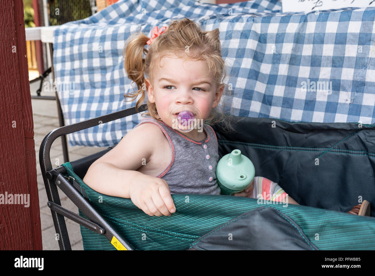 Twenty month old girl waiting in the shade in her wagon Stock Photo