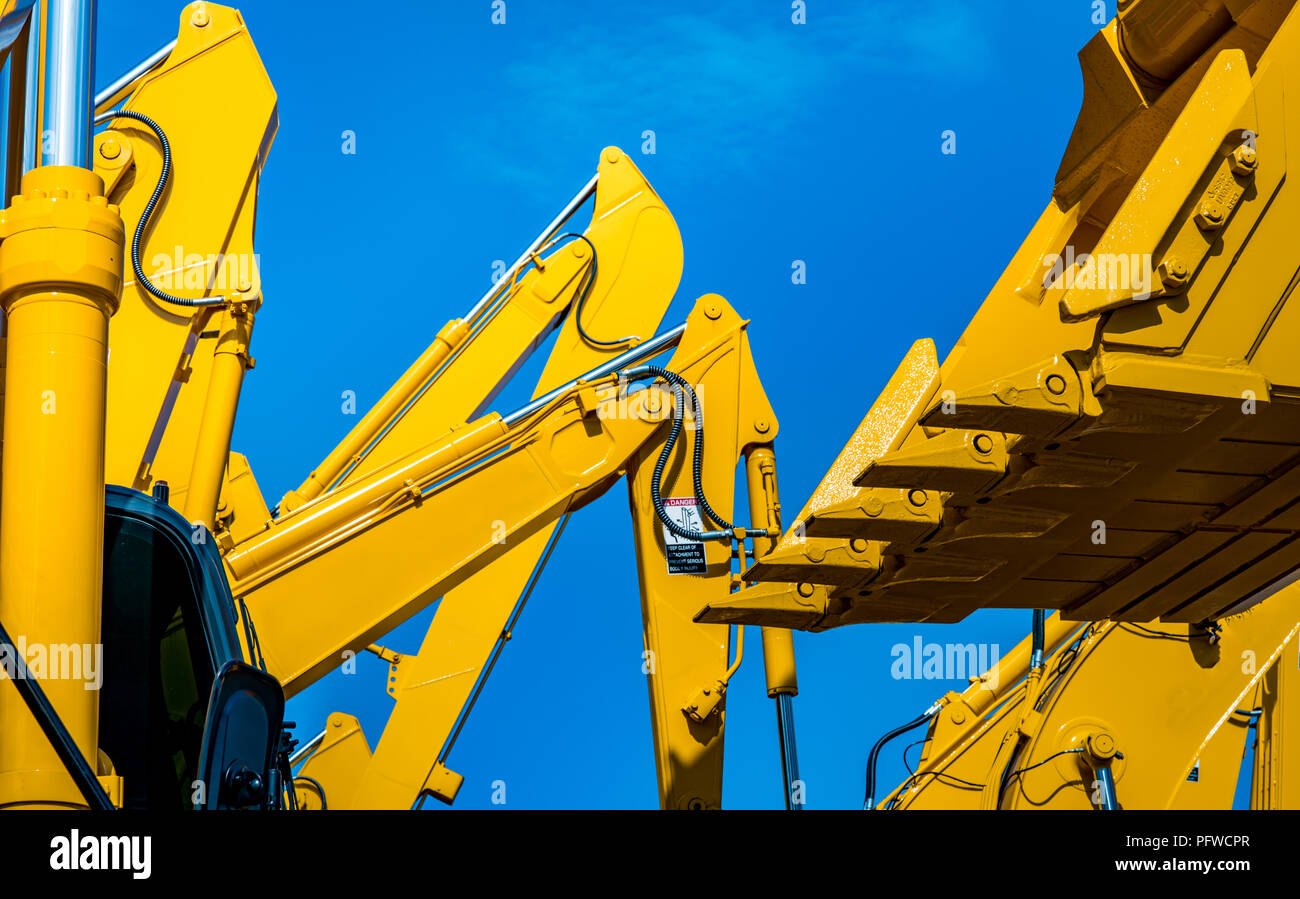 Yellow backhoe with hydraulic piston arm against clear blue sky. Heavy