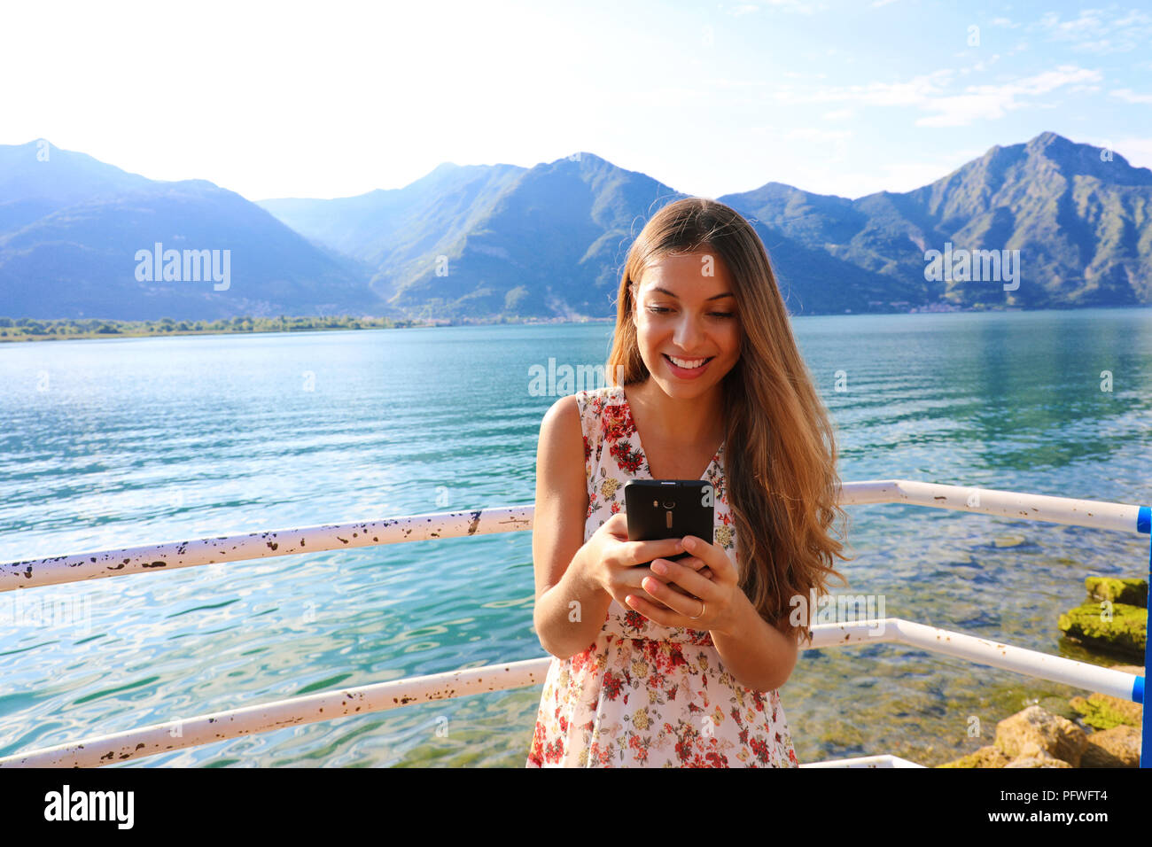 Woman standing near lake and using a smart phone in a sunny summer day Stock Photo