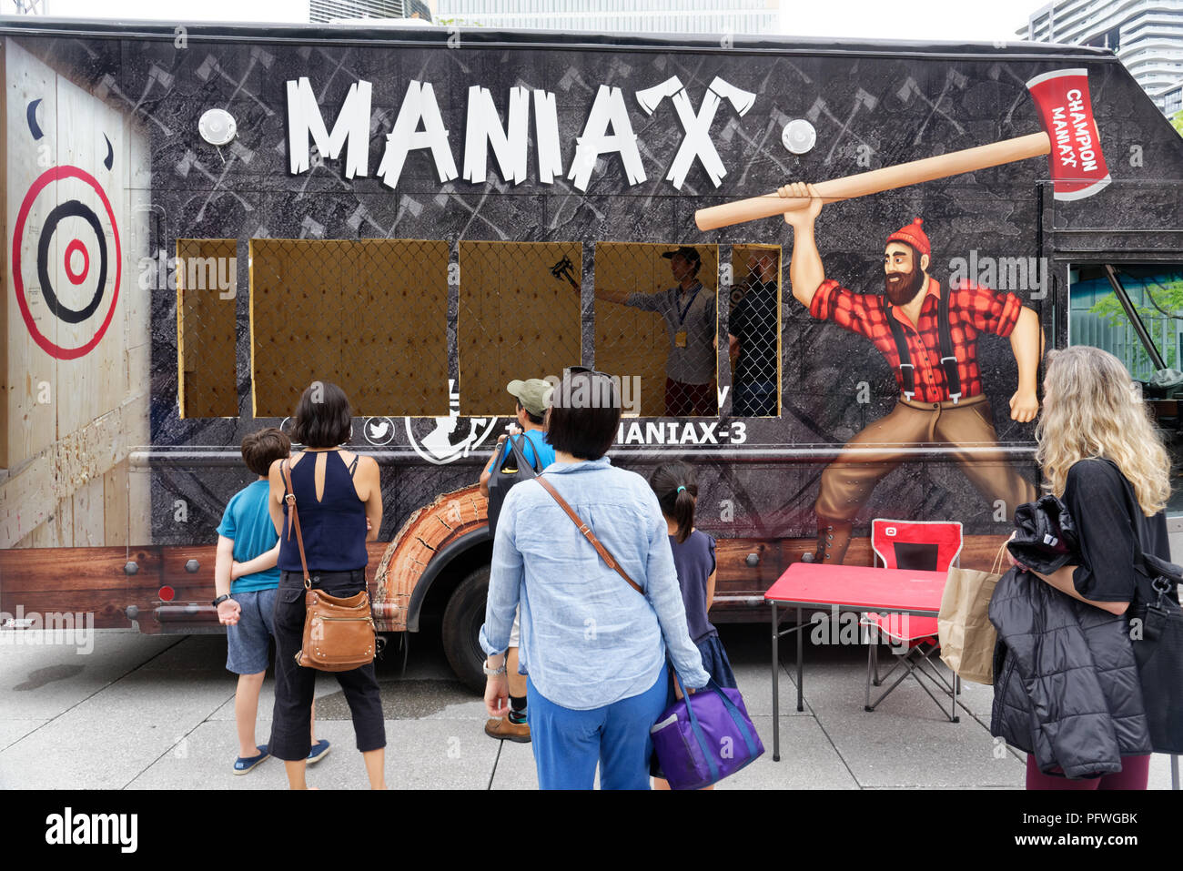 People watching an axe thrower in a Maniax mobile axe throwing game in the back of a truck Stock Photo