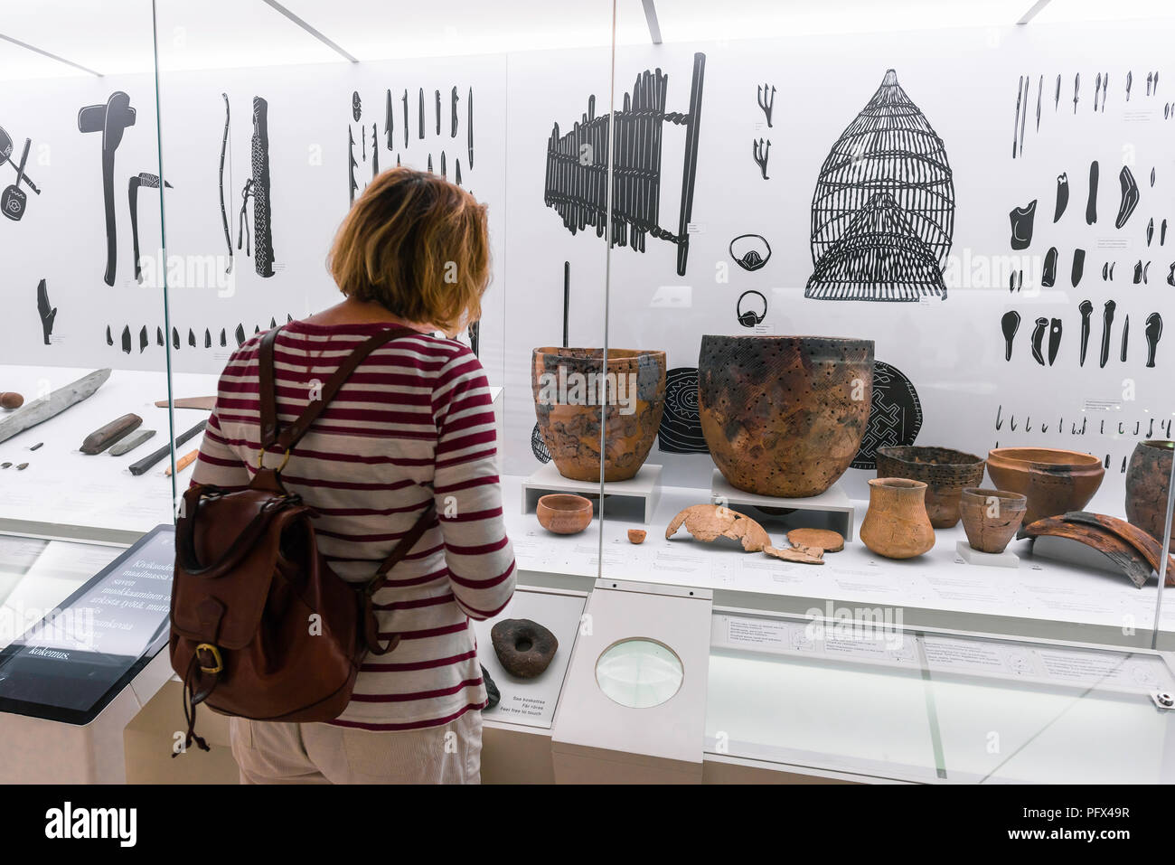 National Museum Of Finland, rear view of a middle aged woman viewing Iron Age pottery in a display case inside the Kansallismuseo in Helsinki. Stock Photo
