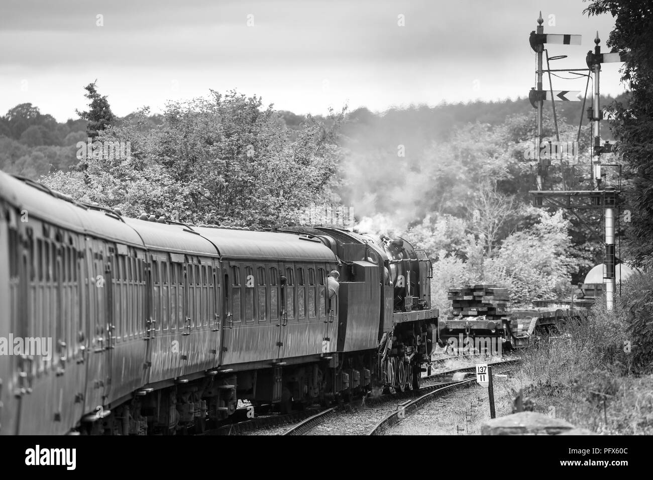 Black & white side view of vintage UK steam train pulling carriages travelling on track past railway signals, Severn Valley Railway heritage line. Stock Photo