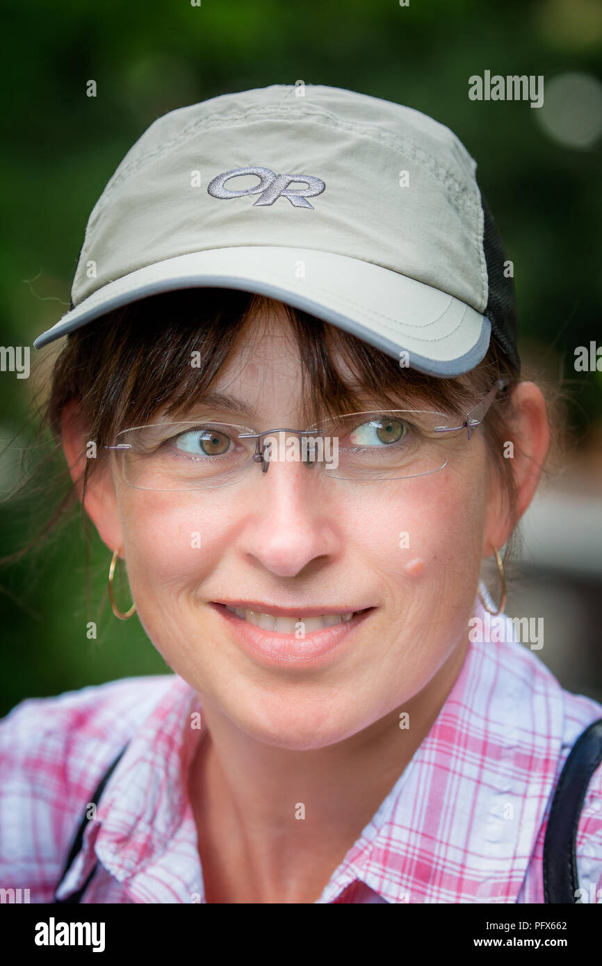 Close-up portrait of trendy 50 year old female in sports cap, with young outlook, casually dressed & glancing to one side, posing with wry smile. Stock Photo
