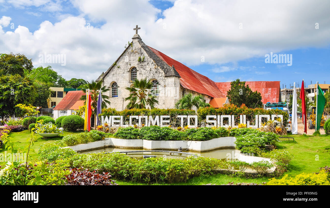 City of Siquijor Welcome Sign, behind which is the Spanish colonial era church Saint Francis de Assisi - Siquijor, Philippines Stock Photo