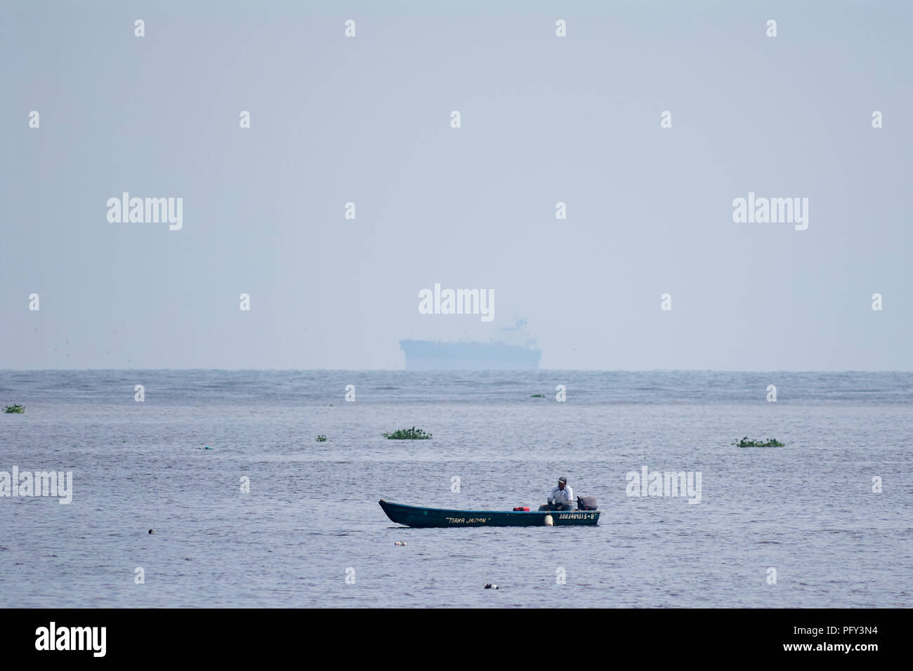 COATZACOALCOS, VER/MEXICO - AUG 18, 2018: A fisherman in a motorboat, fishes with a net at the river mouth. An oil tanker at sea Stock Photo