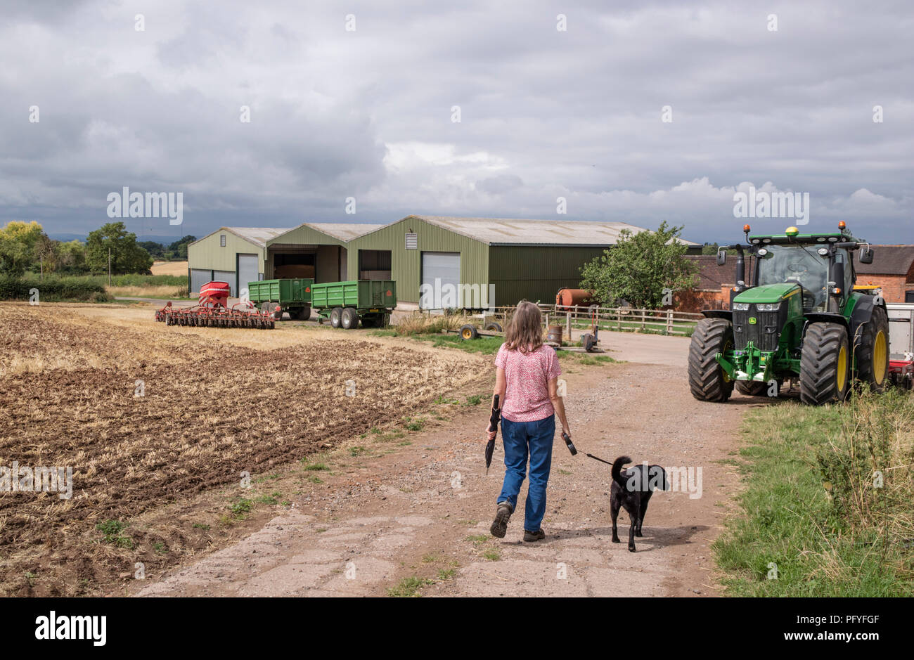 Walking the dog past Farm machinery on an British farm, Britain, UK Stock Photo