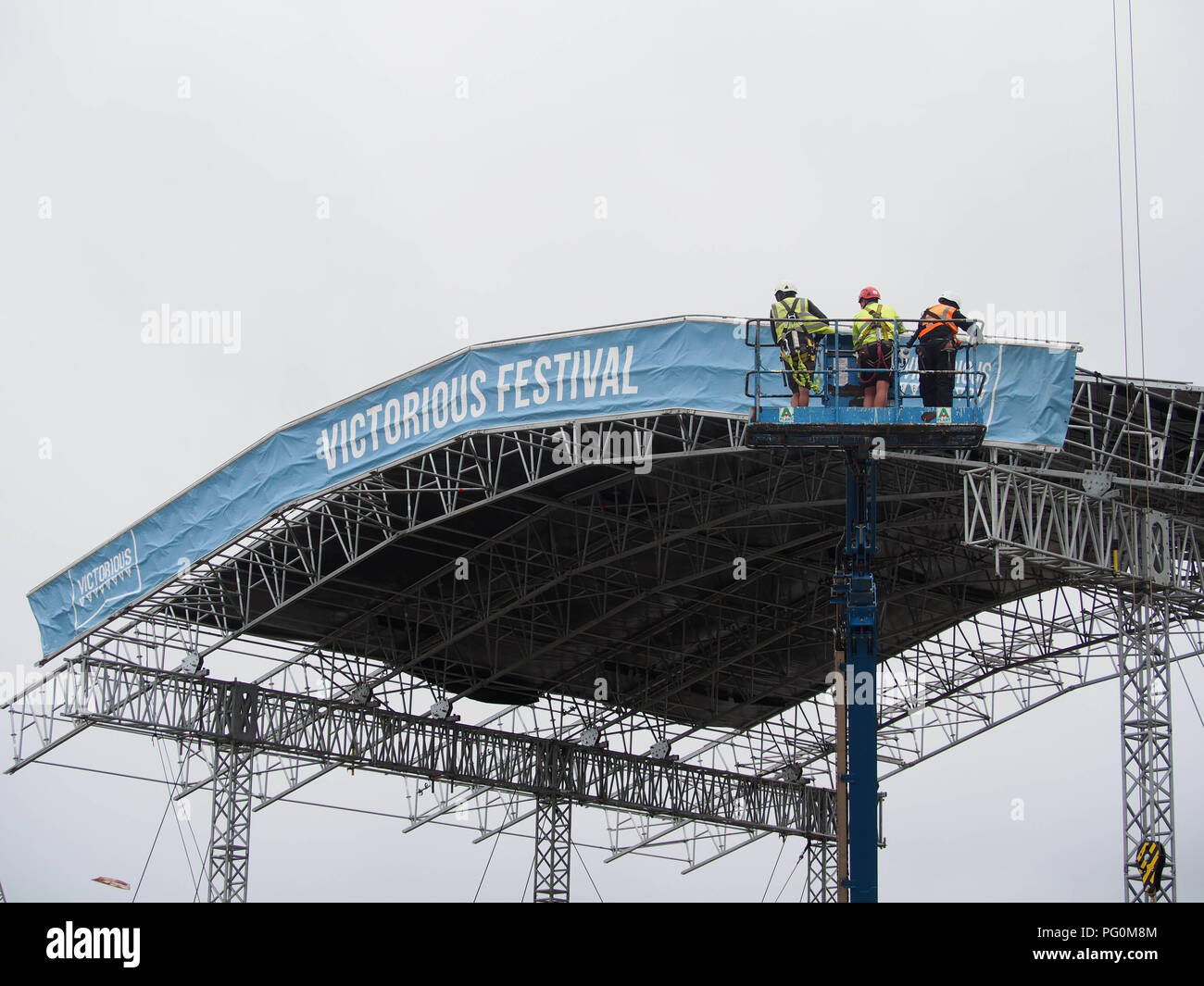 Three workers in a cherry picker assisting in the huilding of a stage for a music festival Stock Photo