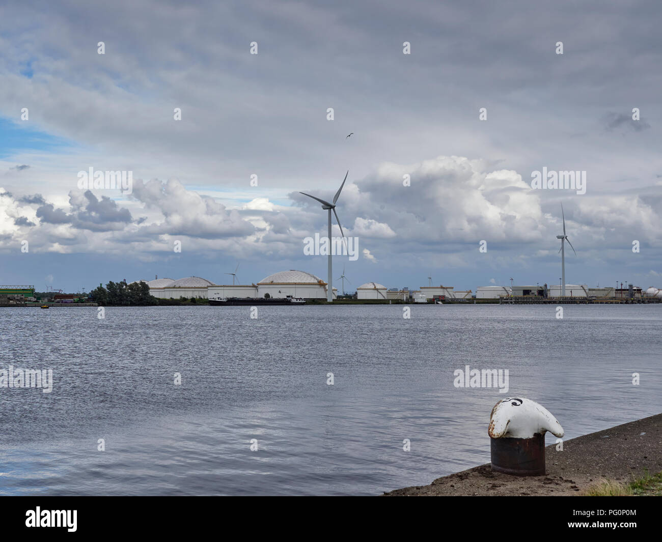 Looking across a part of the North Sea Canal towards the large Liquid Storage Tanks and Wind Turbines in Den Haag in Amsterdam, Holland. Stock Photo