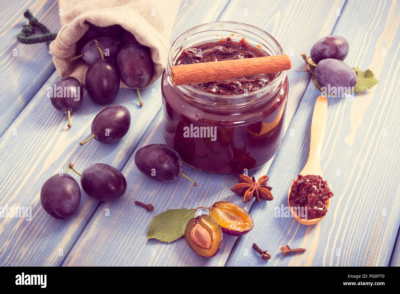 Vintage photo, Fresh plum jam or marmalade in glass jar, ripe fruits and spices on boards, concept of healthy sweet dessert Stock Photo