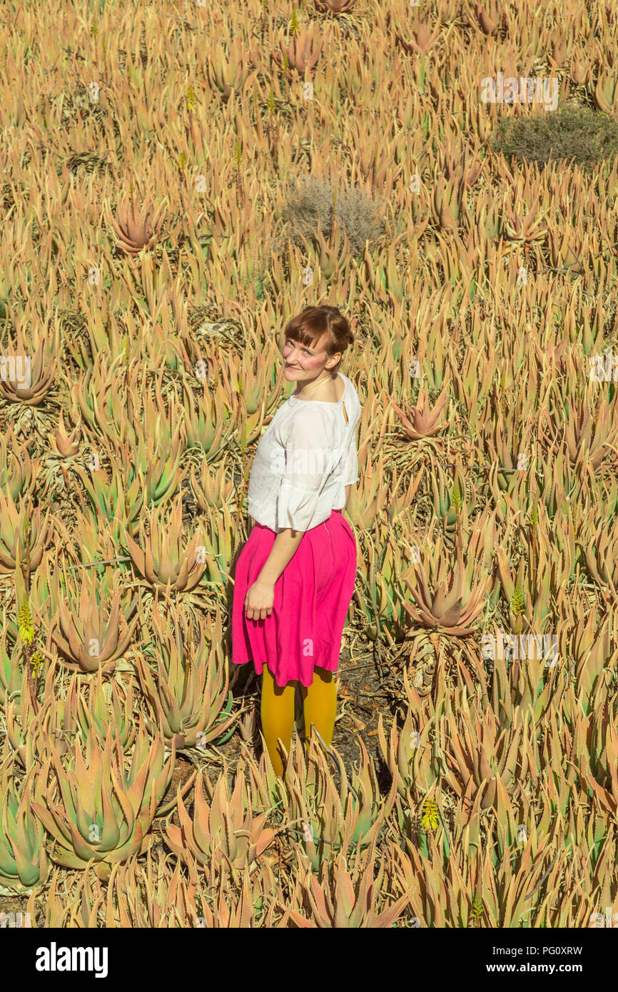 Young woman smiling and looking to the camera in aloe vera Field in Fuerteventura, Canary Islands, Spain. Stock Photo