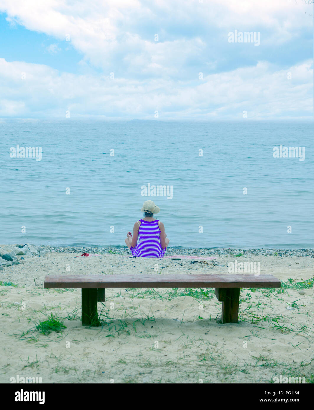 woman meditating on the seashore, in a yoga pose, it seems flying over a bench Stock Photo