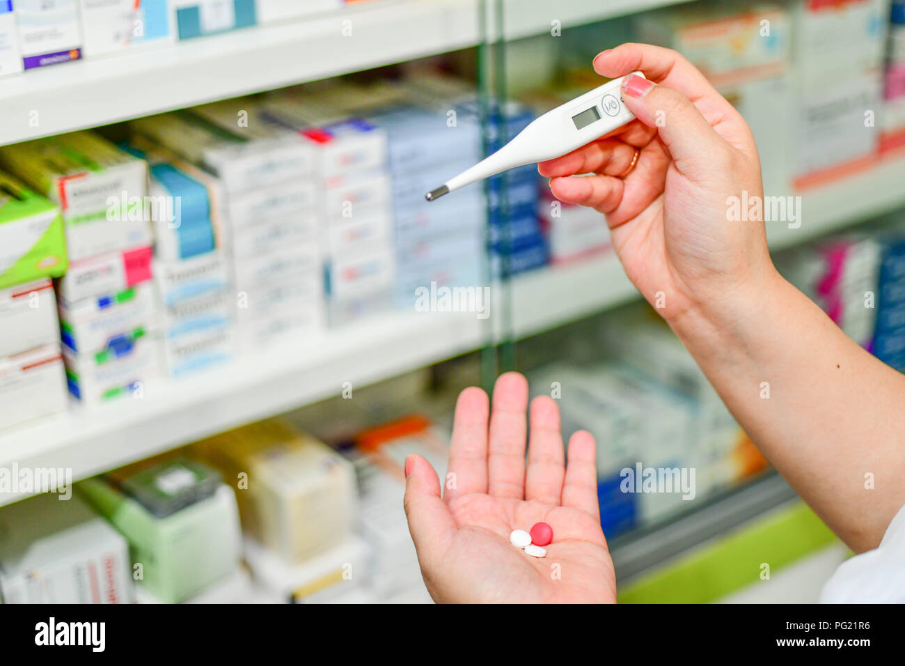 Hand holding digital thermometer at the pharmacy on shelves Stock Photo