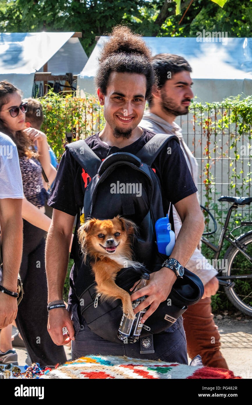 Berlin Mauer Park. Trendy young man  with dog in pouch next to stall of trader Stock Photo