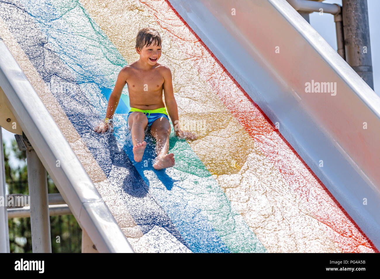 A happy boy on water slide in a swimming pool having fun during summer