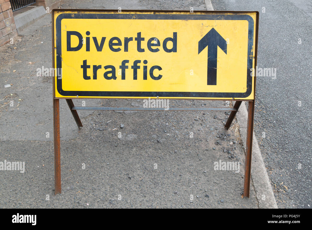 Old, weathered, black and yellow diverted traffic road safety sign on the side of the road. Black text on yellow background with arrow forward Stock Photo