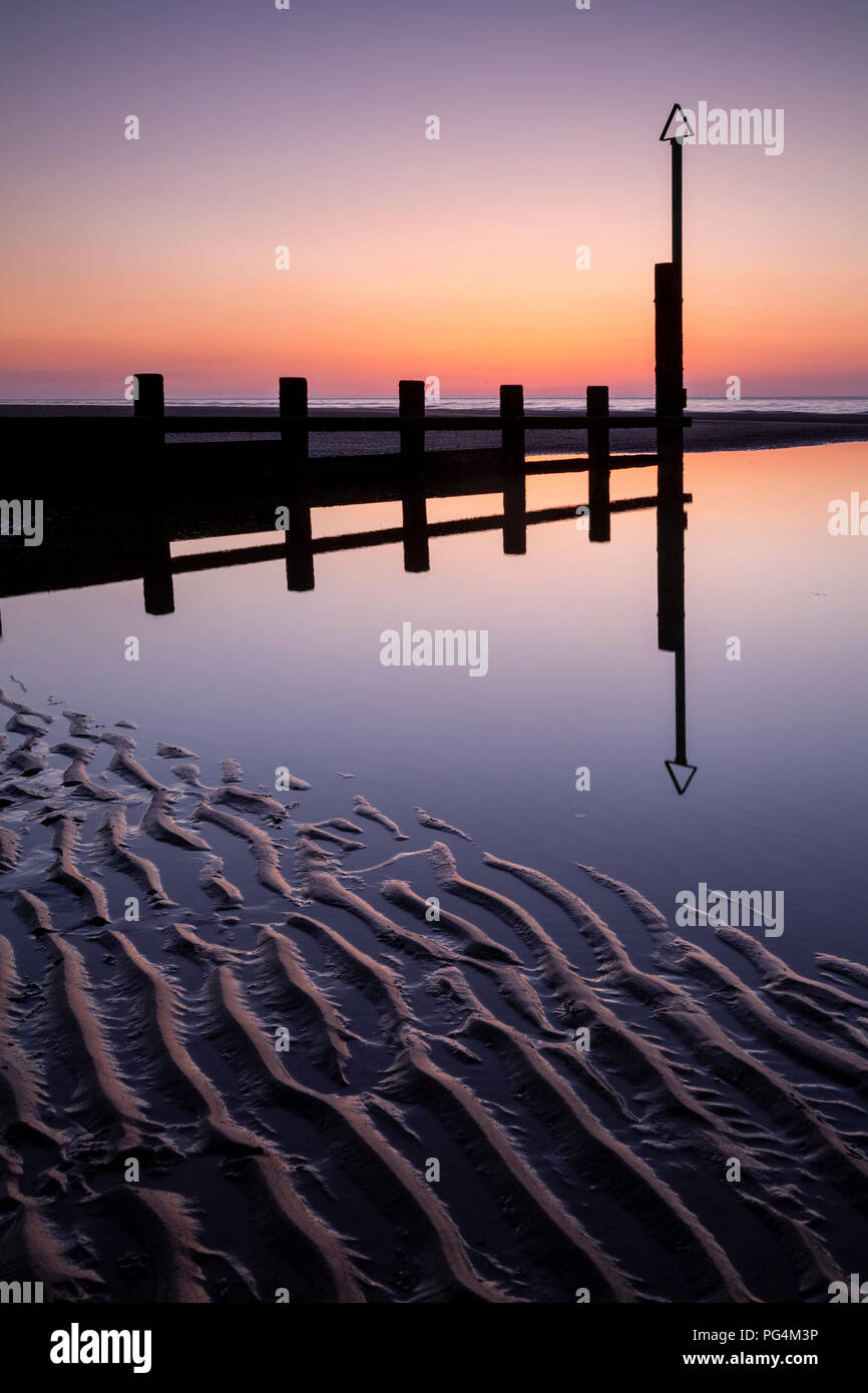 Wooden groynes reflecting in tidal pool on Rhyl beach on the North Wales coast Stock Photo