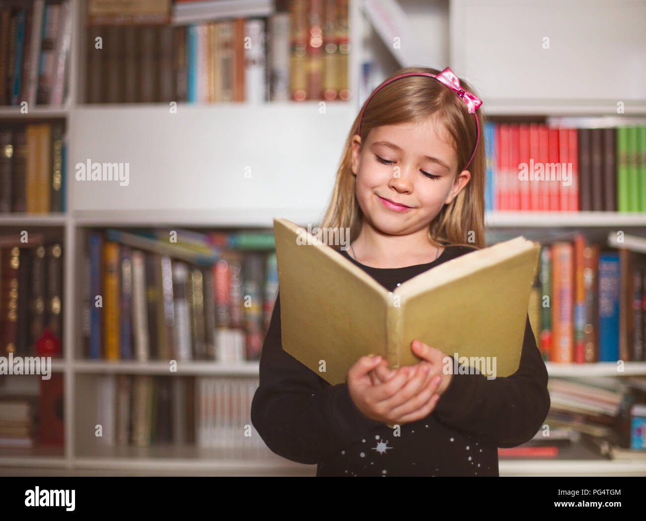 Portrait of the cute little schoolgirl holding book and reading Stock