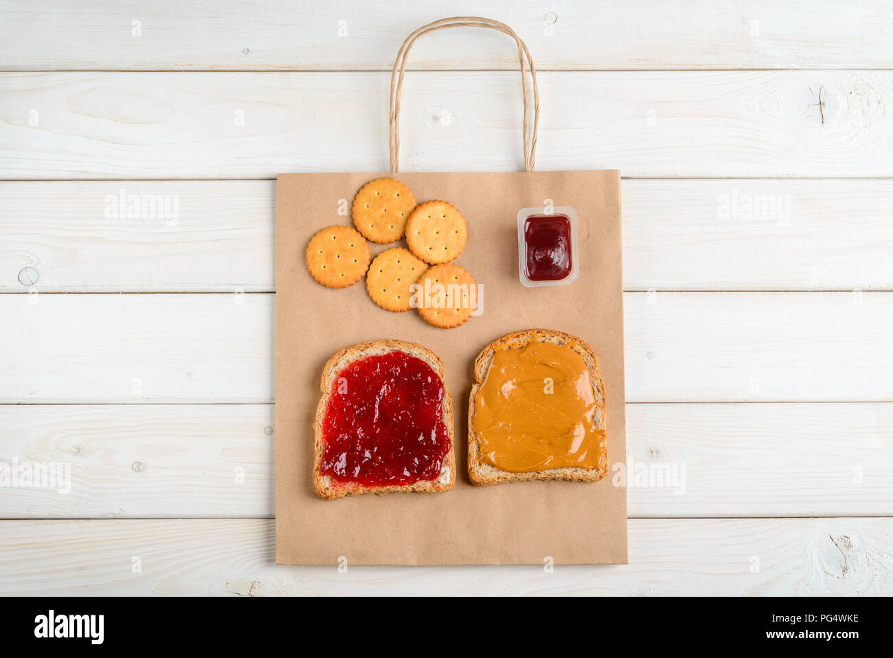 Peanut butter and jam sandwich, paper bag, crackers. Light wooden