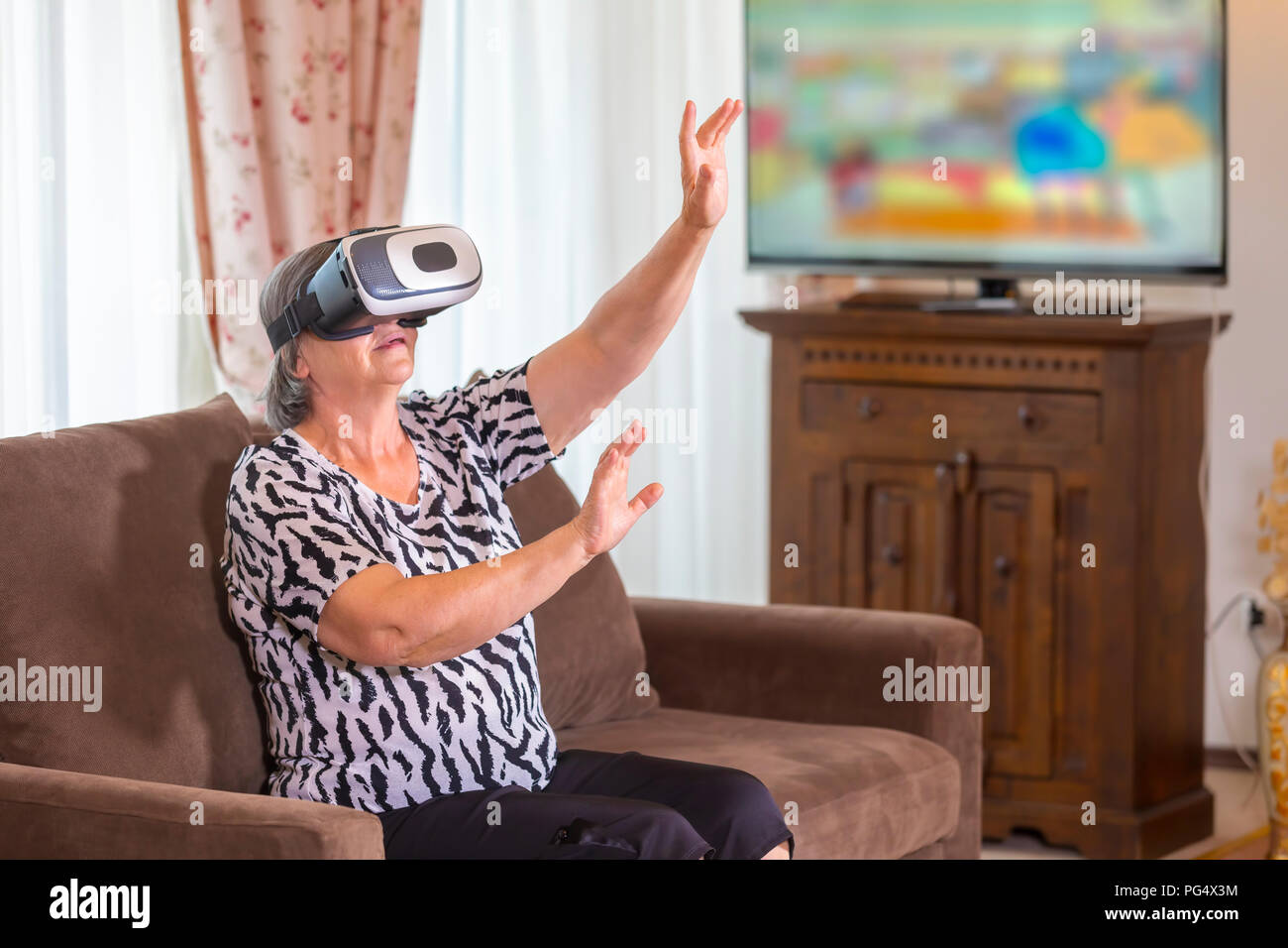 Senior woman with virtual headset or 3d glasses playing videogame at home. Technology, augmented reality, entertainment and people concept. Focus on h Stock Photo