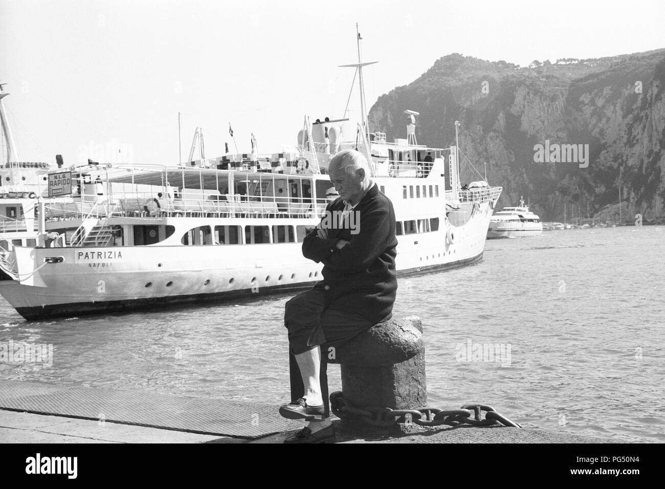 The Czech writer Bohumil Hrabal sits on a bollard in the harbor of the Italian island of Capri. Stock Photo