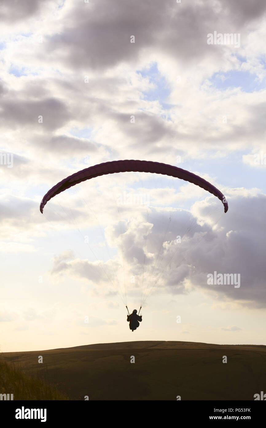 A paraglider is silhouetted against the sky over Edale Valley in the Peak District, Derbyshire. The pilots gain lift from the strong updraft that occu Stock Photo