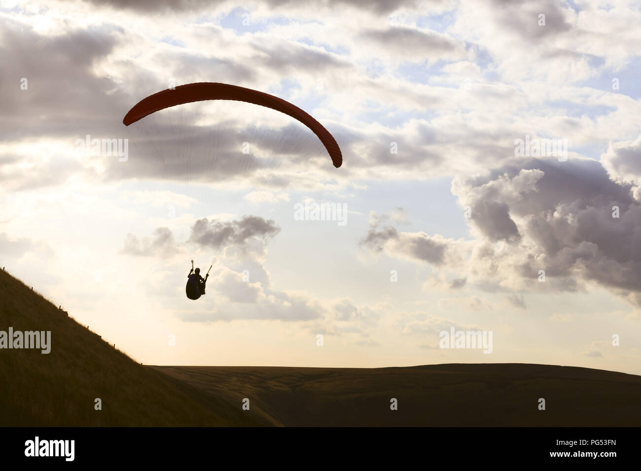 A paraglider is silhouetted against the sky over Edale Valley in the Peak District, Derbyshire. The pilots gain lift from the strong updraft that occu Stock Photo