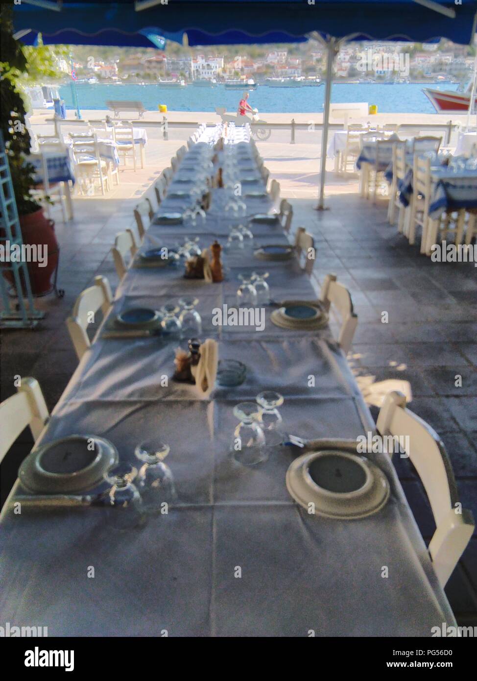 Greece, the beautiful island of Poros, near Athens. Tables in a row set for dinner, early in the evening at a traditional taverna. Stock Photo
