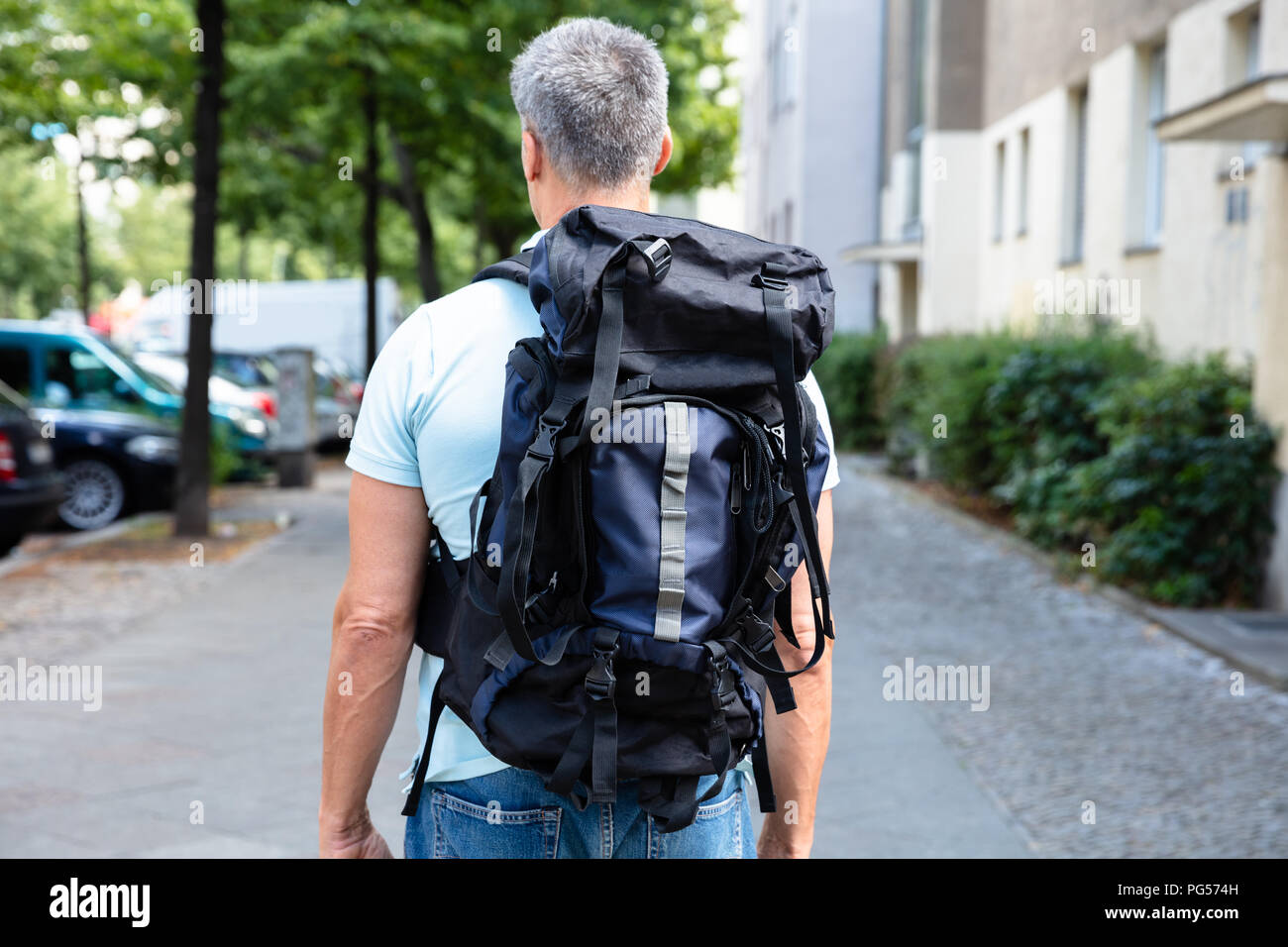 Rear View Of A Man With Backpack Walking On Pavement Stock Photo - Alamy