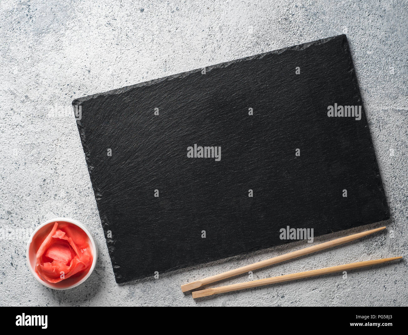 Empty slate plate on gray cement background with chopsticks and pickled ginger. Copy space. Top view or flat-lay. Concept for restaurant and delivery sushi and rolls Stock Photo