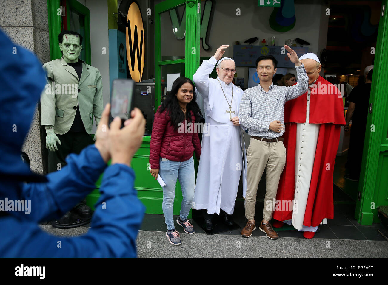 Tourists pose for photos with a newly unveiled wax work of Pope Francis (left) and the waxwork of Pope John Paul II at the National Wax Museum Plus in Dublin where they also unveiled a newly refurbished original 1979 Pope Mobile ahead of Pope Francis&Otilde; Visit To Ireland. Stock Photo