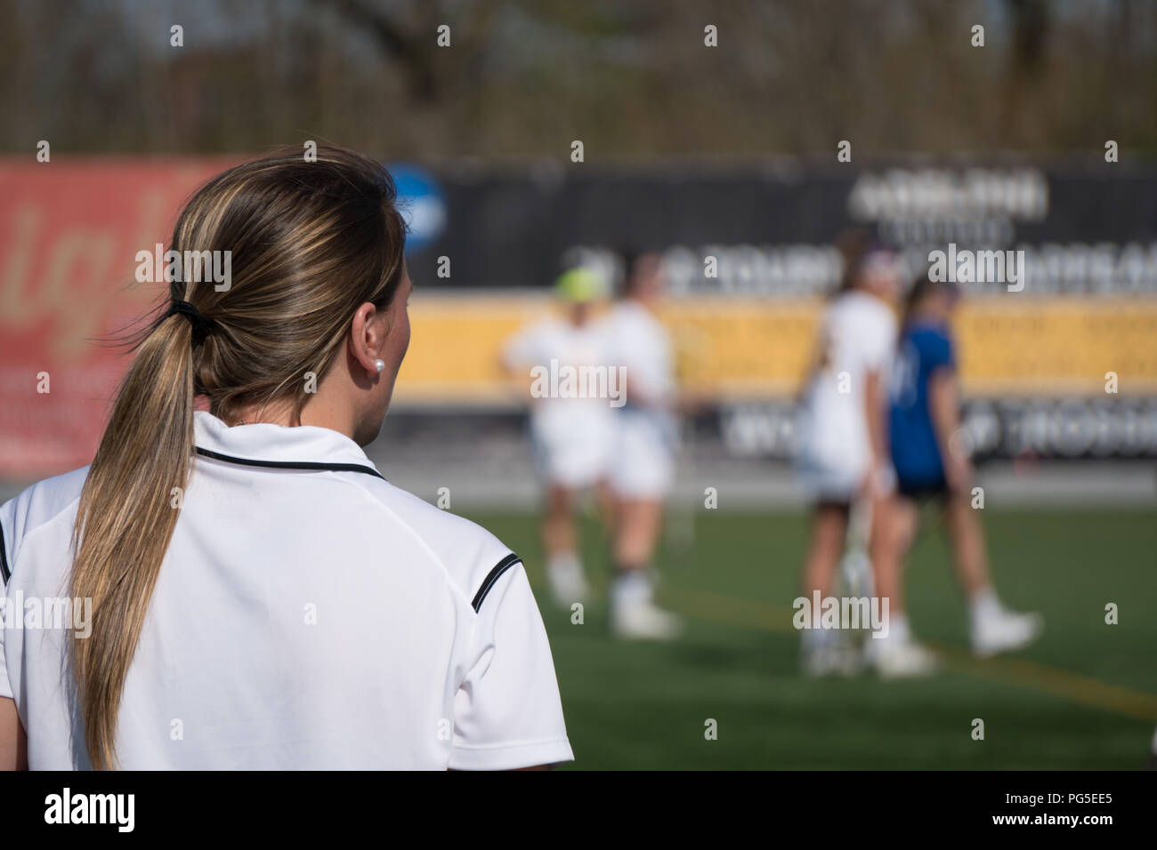 Over the shoulder female head coach on sidelines yelling play call to girl soccer players on field competing tournament match game on bright summer da Stock Photo