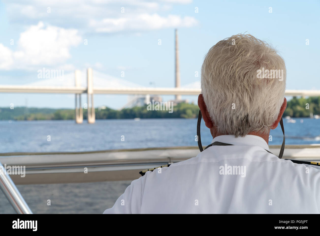 Over the shoulder POV view of a boat captain sailing down a river. Charting navigation path under bridge and past smoke stack factory on a clear summe Stock Photo