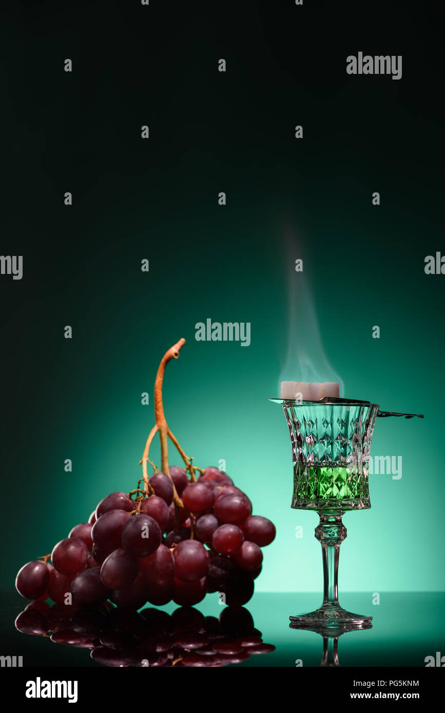 glass of burning absinthe with sugar and grapes on dark blue background Stock Photo
