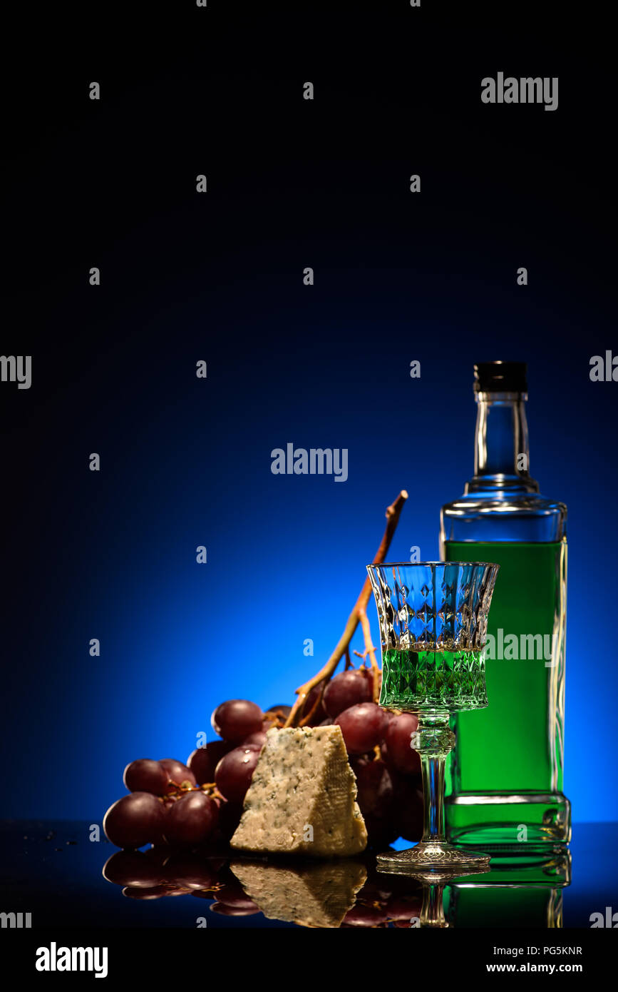 close-up shot of absinthe with grapes and dorblu cheese on mirror surface on dark blue background Stock Photo