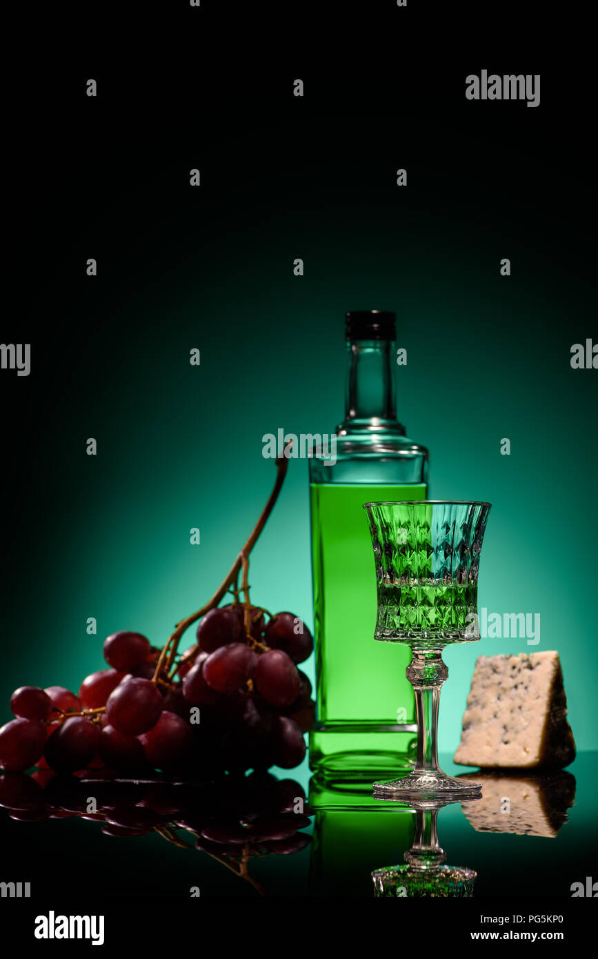 close-up shot of absinthe with grapes and cheese on mirror surface on dark blue background Stock Photo