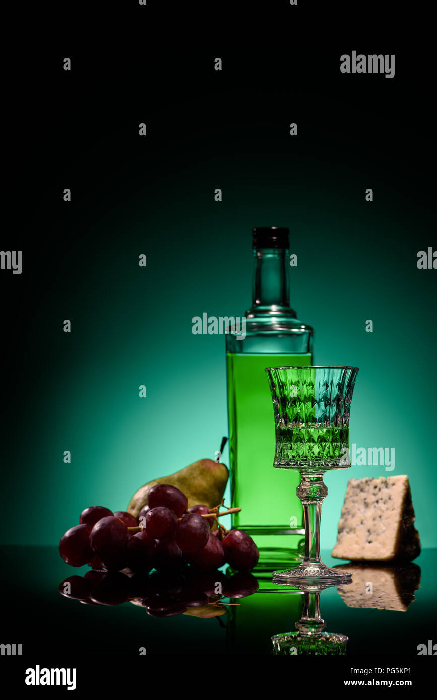 close-up shot of absinthe with pear, grapes and cheese on mirror surface on dark blue background Stock Photo