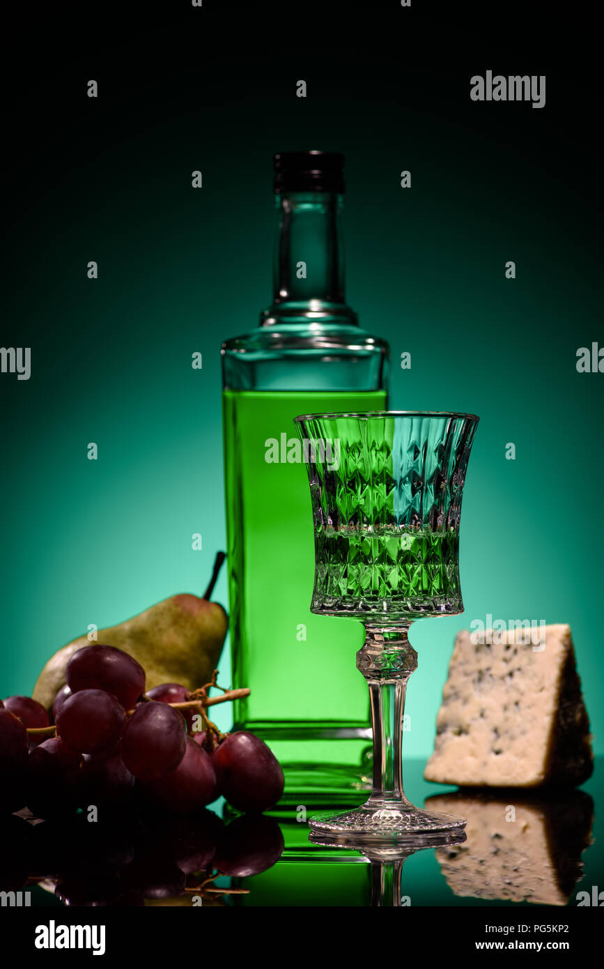 close-up shot of absinthe with fruits and cheese on mirror surface on dark blue background Stock Photo
