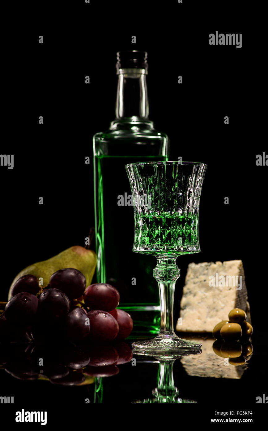 close-up shot of absinthe with ripe fruits and cheese on mirror surface on black Stock Photo