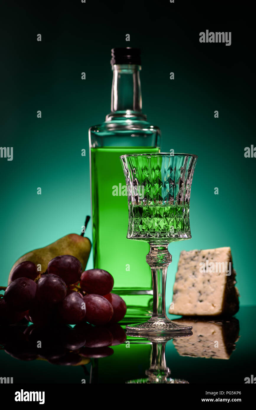 close-up shot of absinthe with ripe fruits and cheese on mirror surface on dark blue background Stock Photo