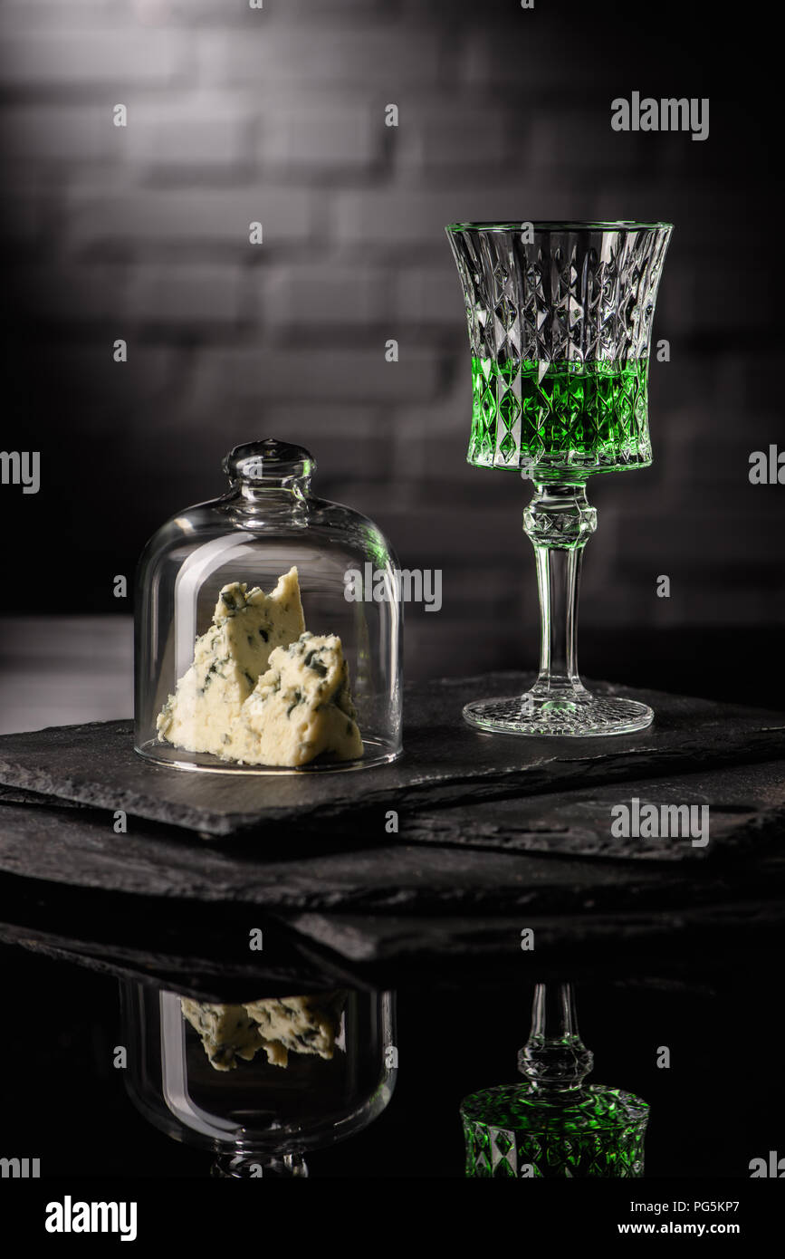 close-up shot of glass of absinthe with slice of cheese on dark brick wall background Stock Photo