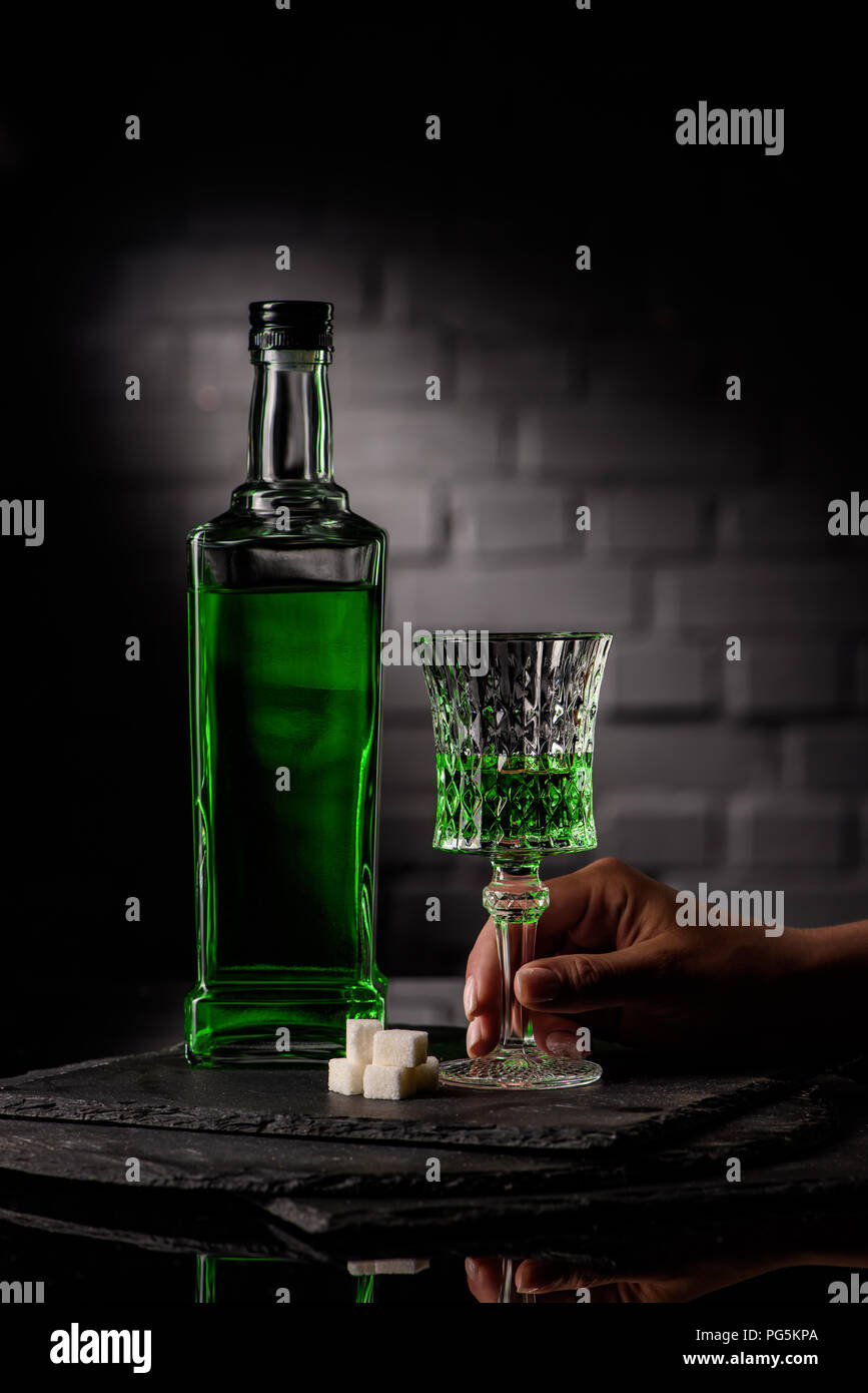 cropped shot of woman holding glass of absinthe on dark brick wall background Stock Photo